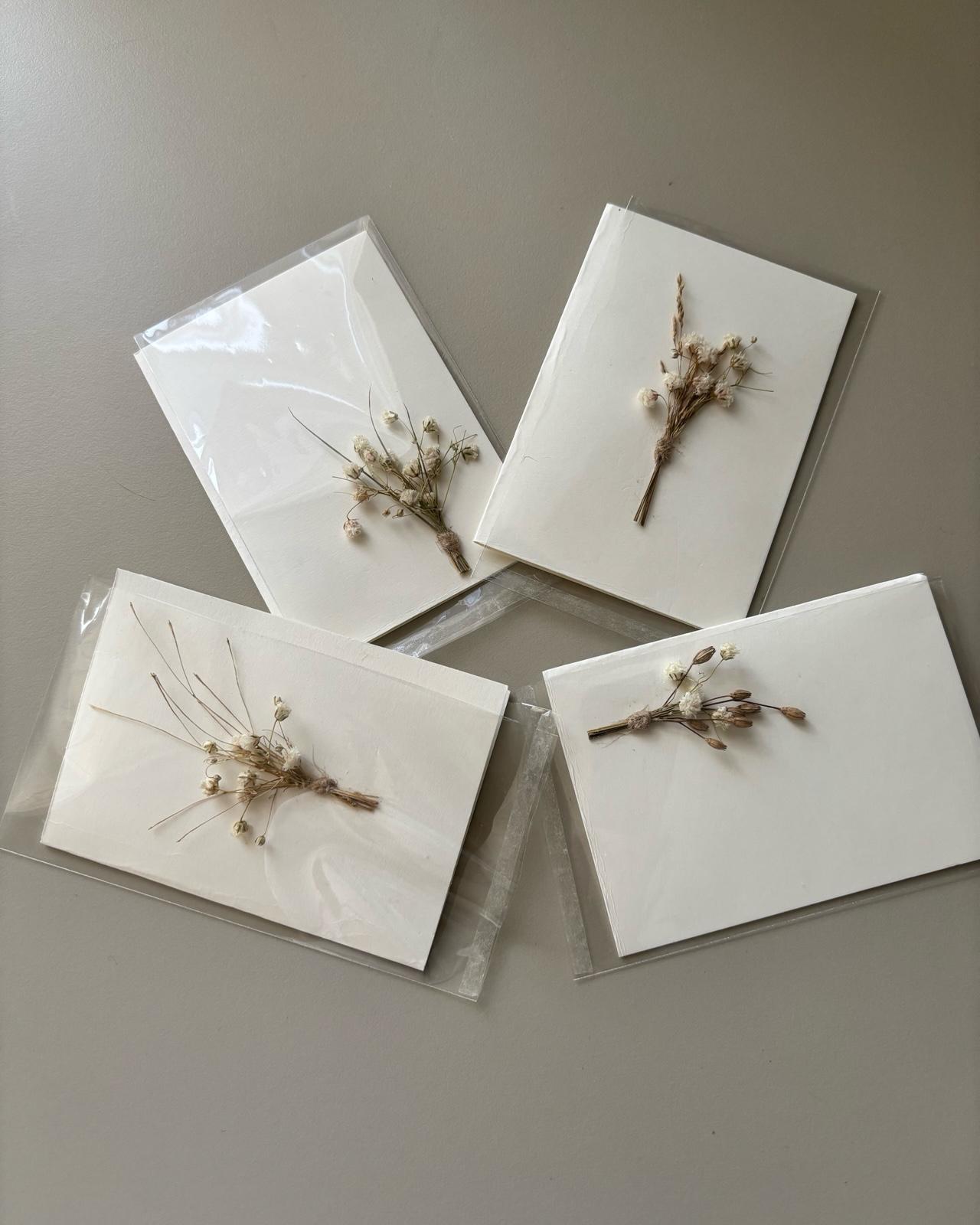Four white cards with dried flowers on a gray surface