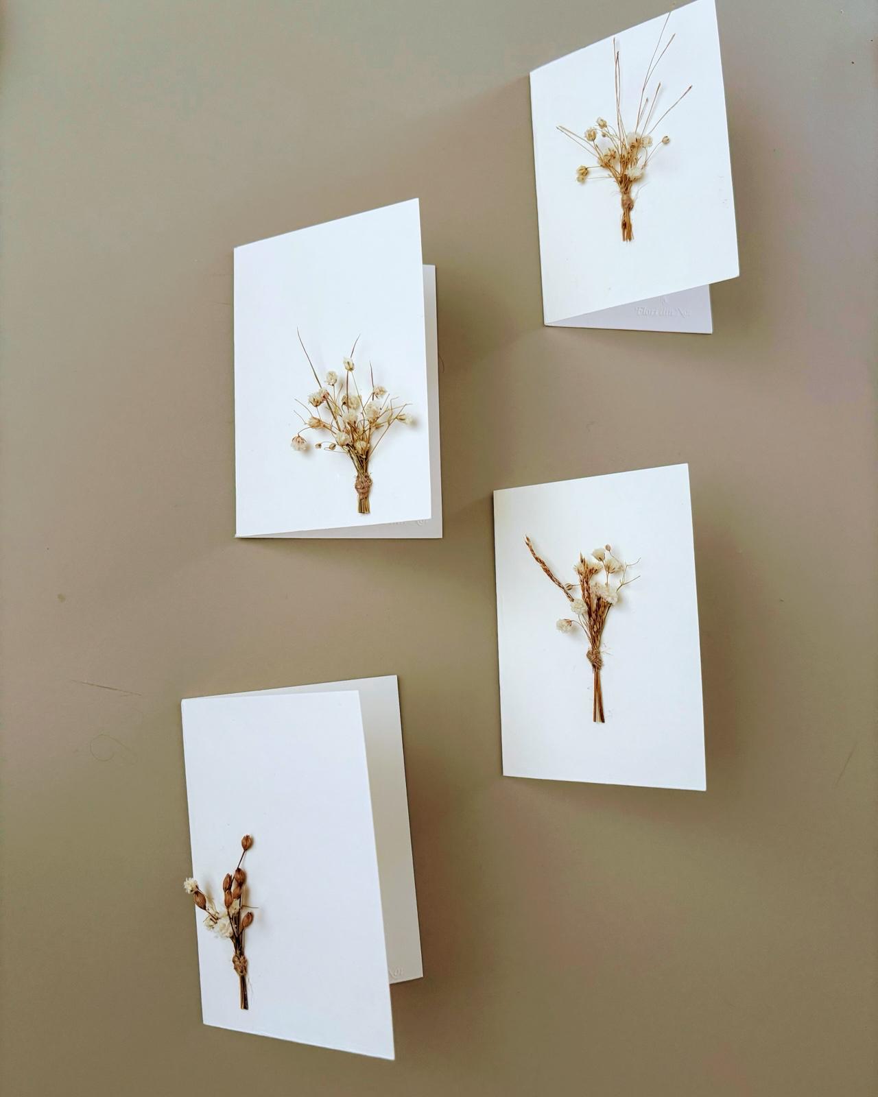 Four white cards with dried flowers on a gray surface