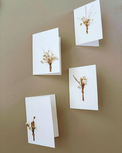 Four white cards with dried flowers on a gray surface